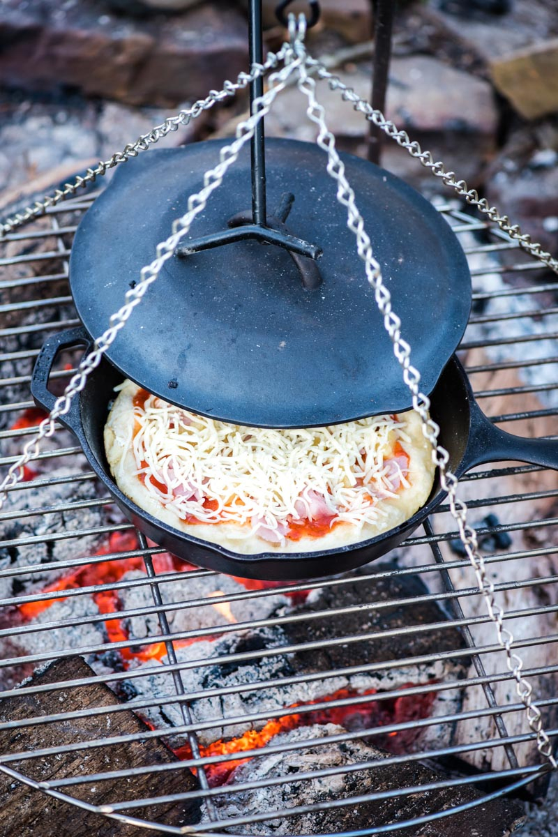 making campfire pizza from scratch in cast iron skillet over campfire