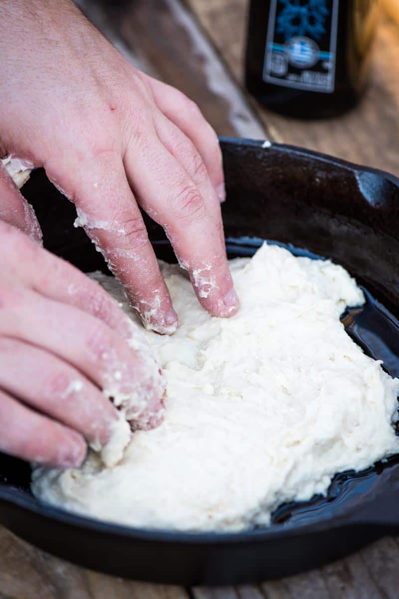 pressing easy pizza dough into cast iron skillet