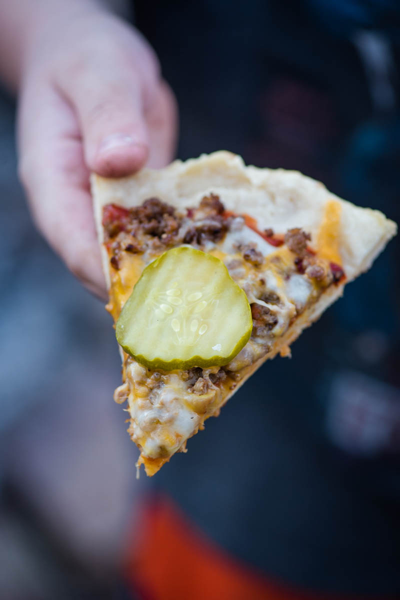 hand holding slice of homemade grilled cheeseburger pizza