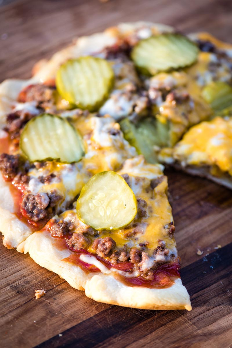 sliced cheeseburger pizza with one slice missing on wooden cutting board