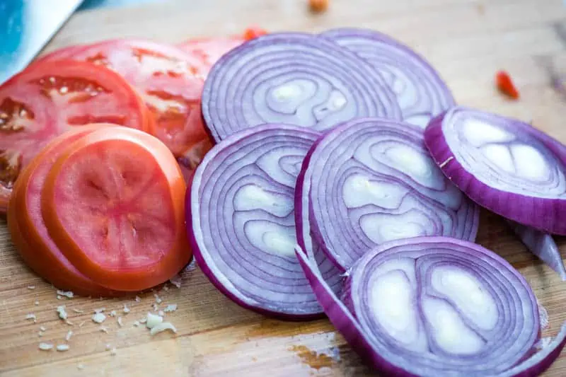 sliced tomatoes and red onions on cutting board for cheeseburger recipe