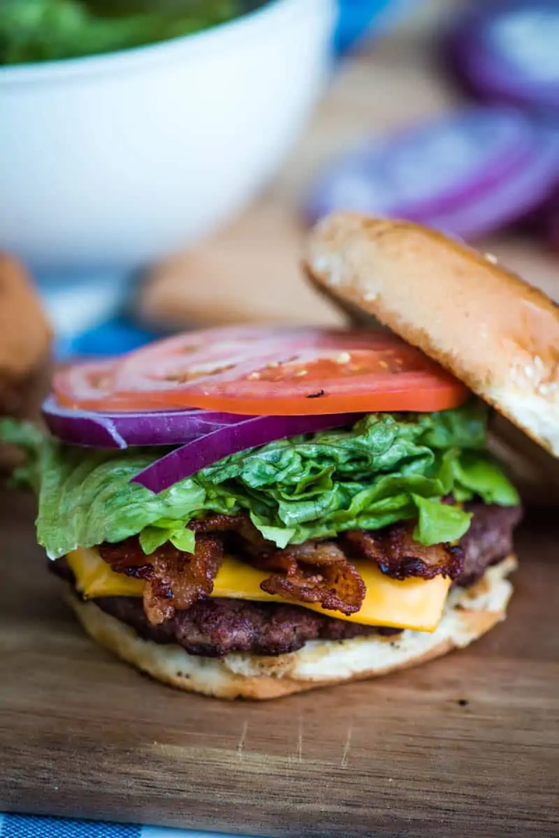 open faced bacon burger with lettuce, red onion, and tomato slices on wood cutting board