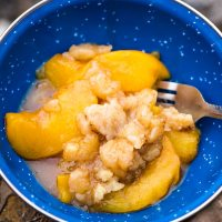 peach cobbler recipe dished up in blue enamel camping bowl with fork