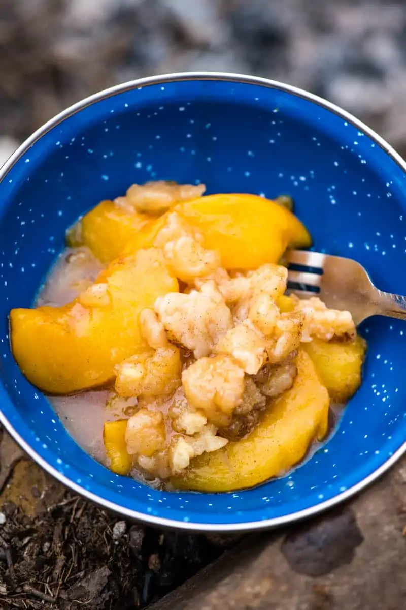 peach cobbler recipe dished up in blue enamel camping bowl with fork