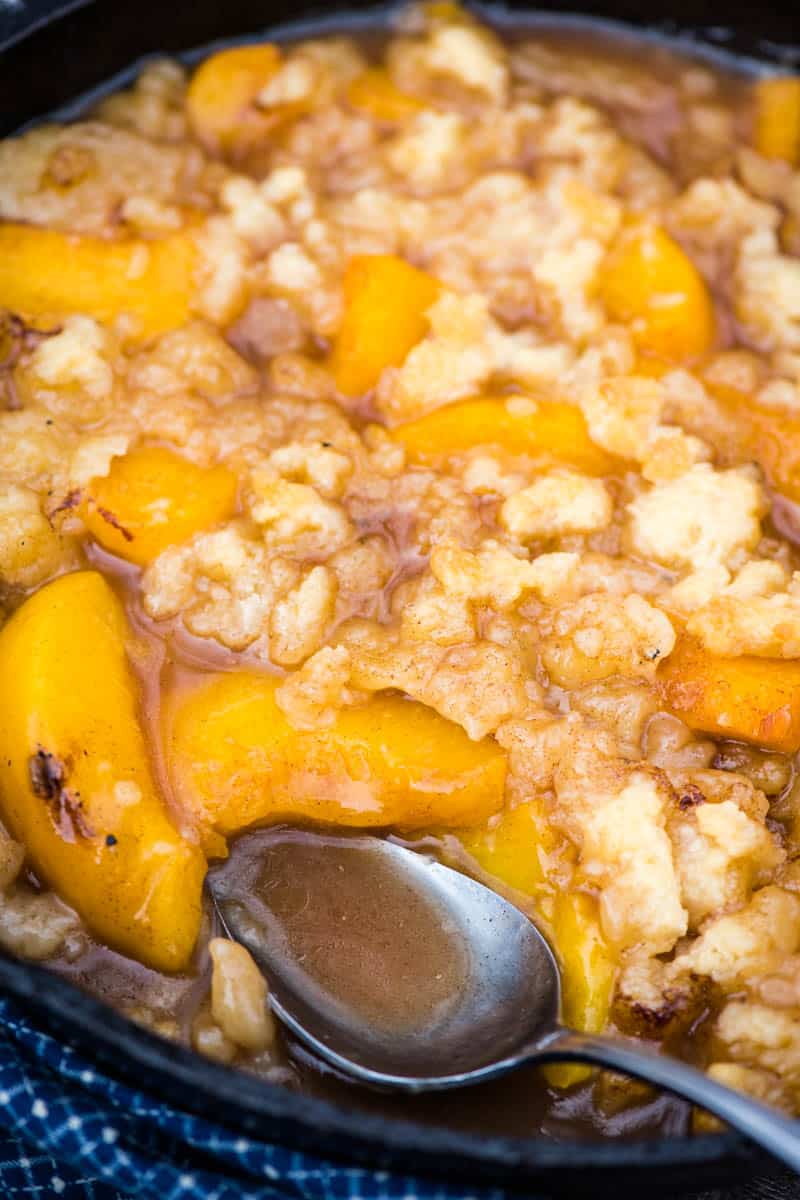 campfire peach cobbler in a cast iron skillet with large serving spoon