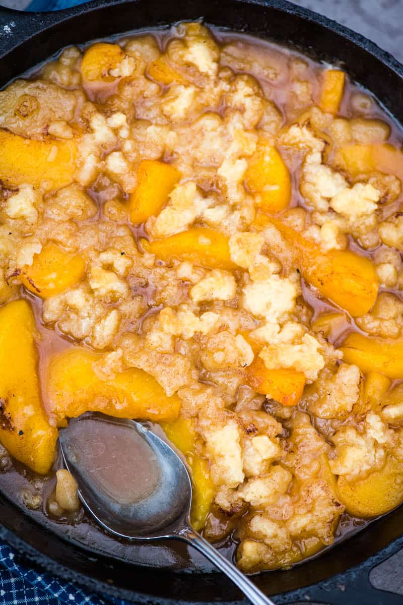cooked peach crumble in a cast iron skillet with serving spoon