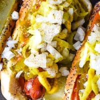 Grilled Chicago hot dog with dill pickle, tomato slices, mustard, pickle relish, white onion, and celery salt on baking sheet