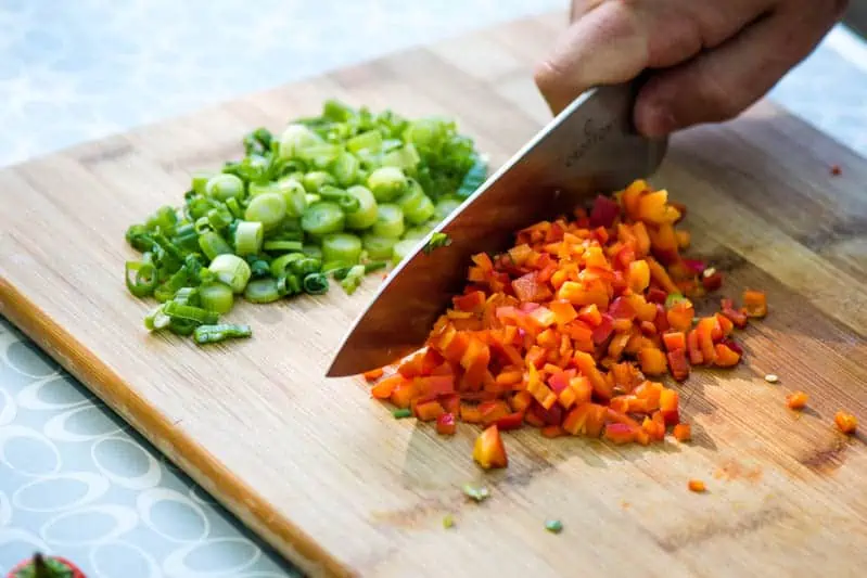 chopping green onions and red bell peppers on wooden cutting board for grilled tuna melt recipe