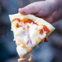 hand holding slice of Hawaiian pizza cooked over a campfire