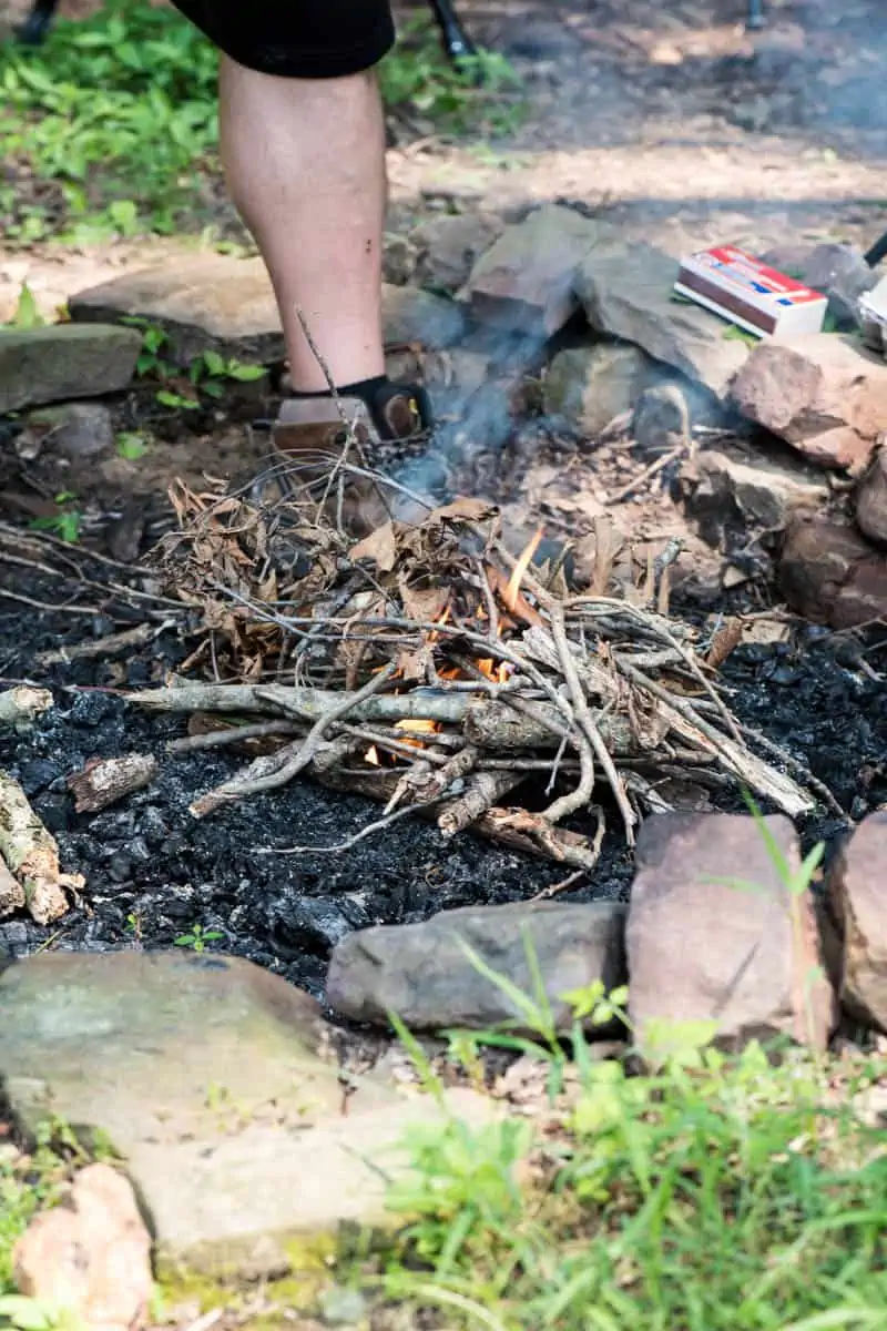 man adding kindling to easy fire starter in campfire pit