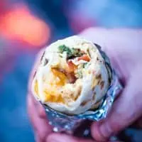 hands holding bacon, egg, and cheese camping breakfast burrito wrapped in foil