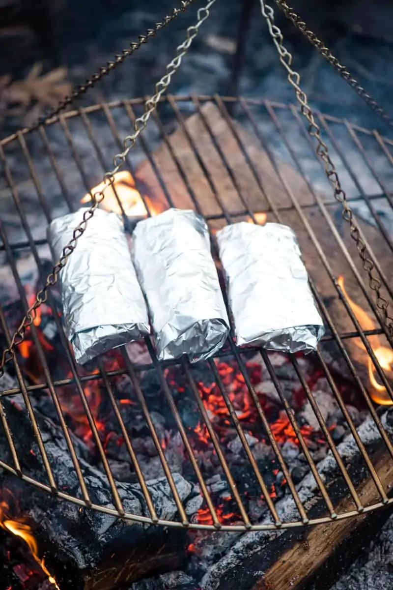 cooking campfire breakfast burritos in foil over the campfire on a tripod grill