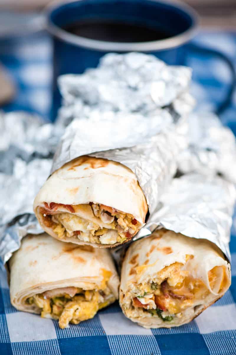 stack of breakfast burritos, wrapped in foil, on blue gingham picnic table