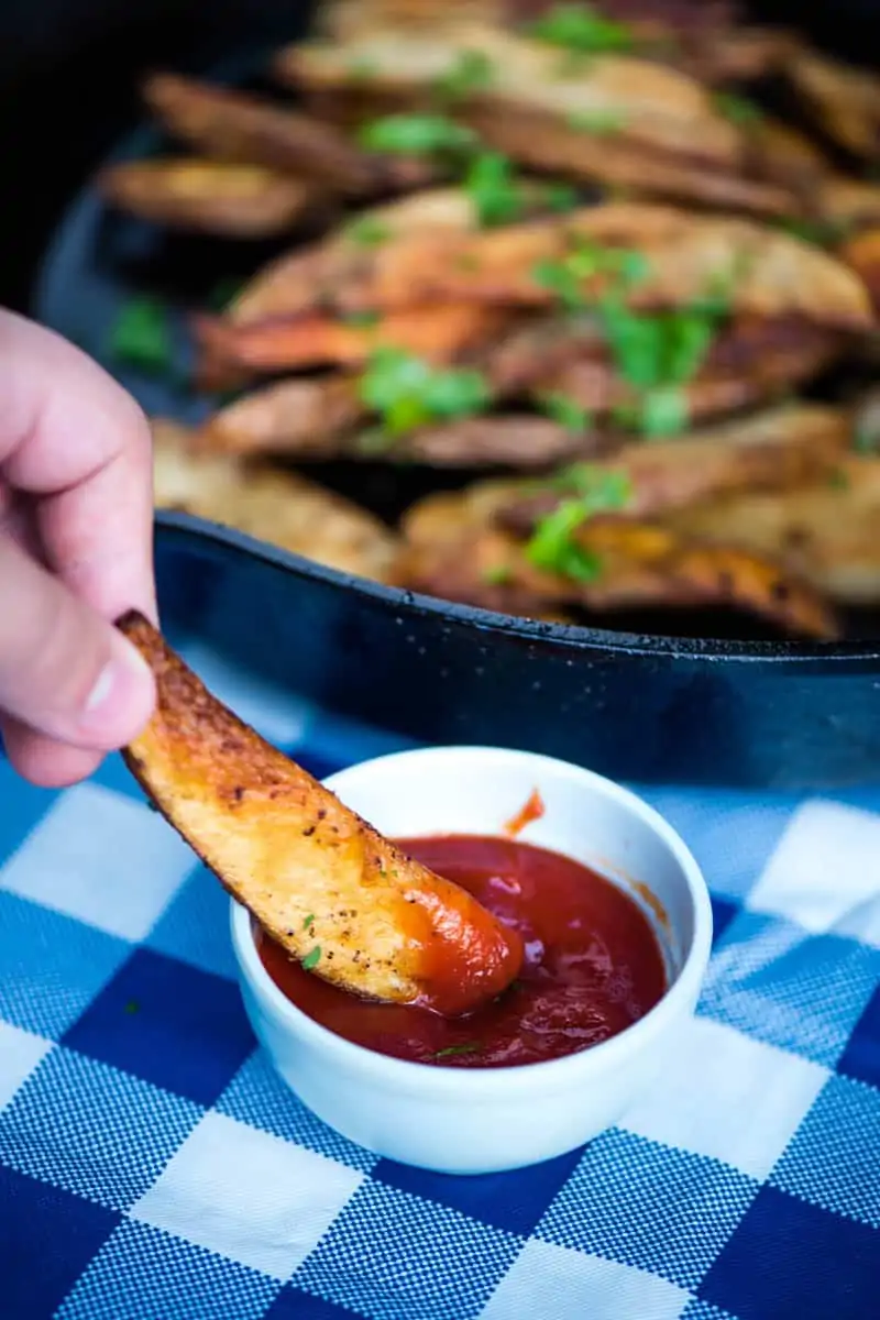 dipping potato wedges in ketchup in small blue bowl