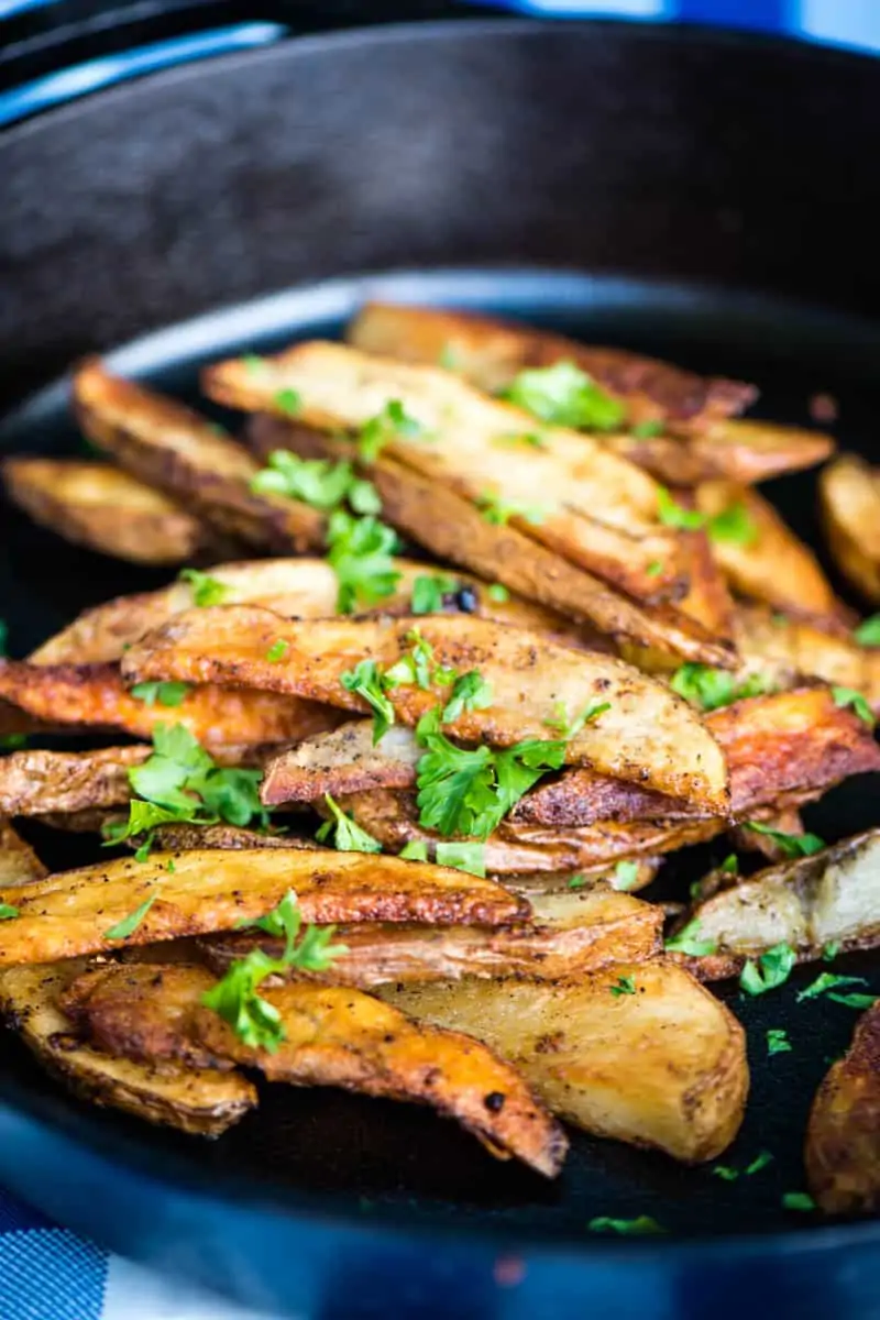 golden brown steak cut fries, sprinkled with parsley, in cast iron skillet