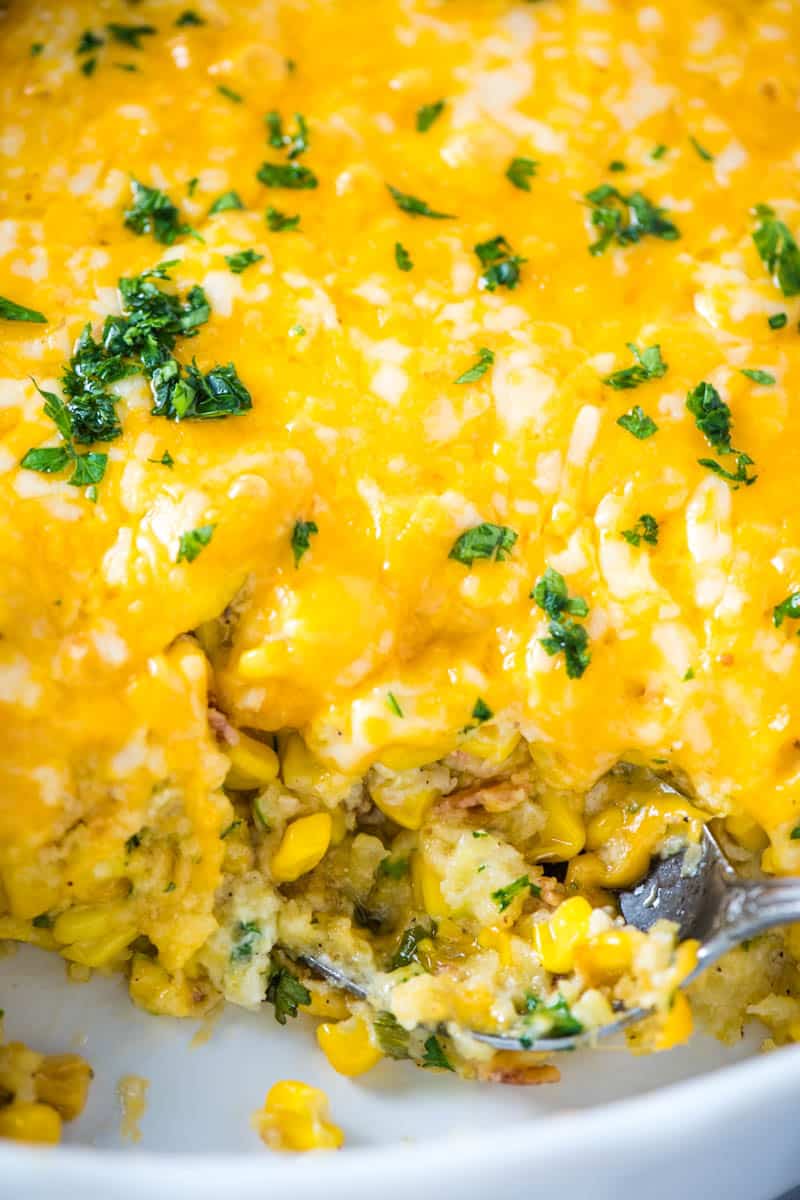 cheesy corn casserole with Jiffy mix in white baking dish with serving spoon