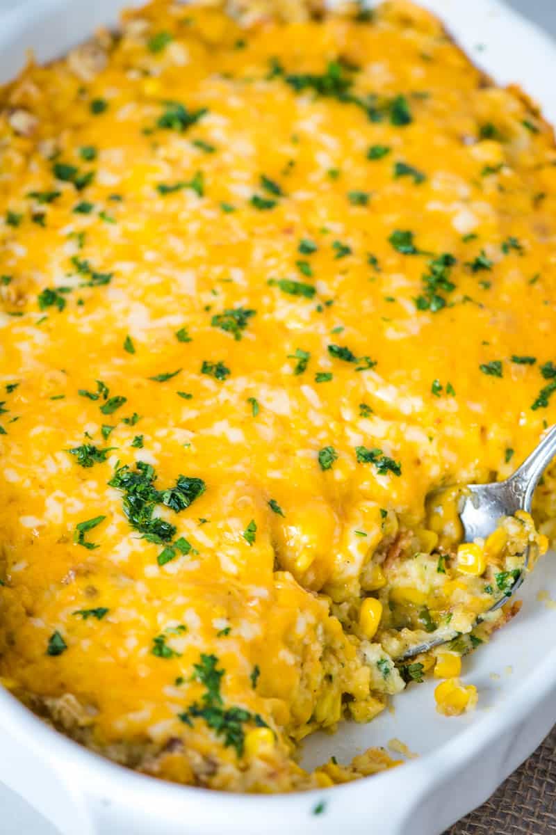 corn casserole with bacon in large white casserole dish with serving spoon