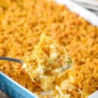 large spoonful of cheesy hash brown casserole with Corn Flakes above blue baking dish