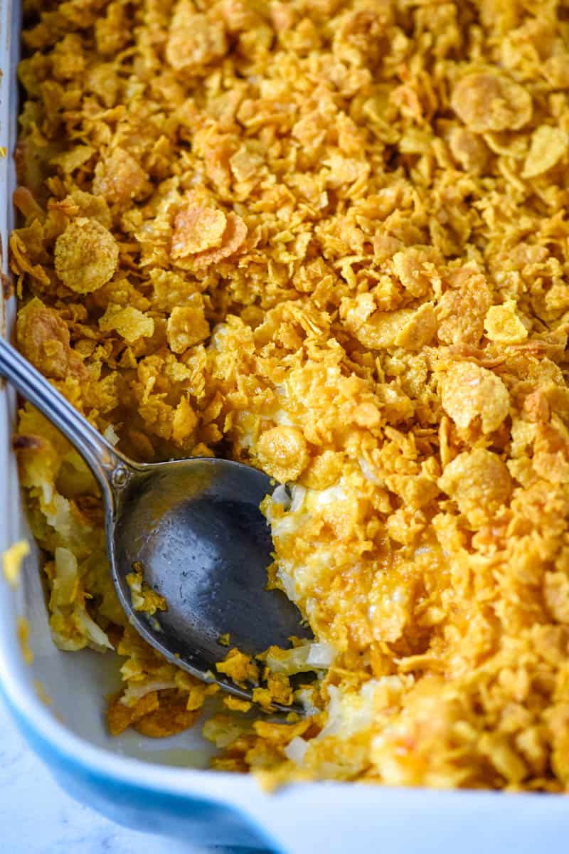 funeral potatoes in blue baking dish with large serving spoon