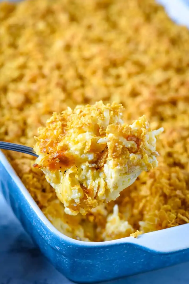 scoop of hash brown casserole in large spoon over blue baking dish 
