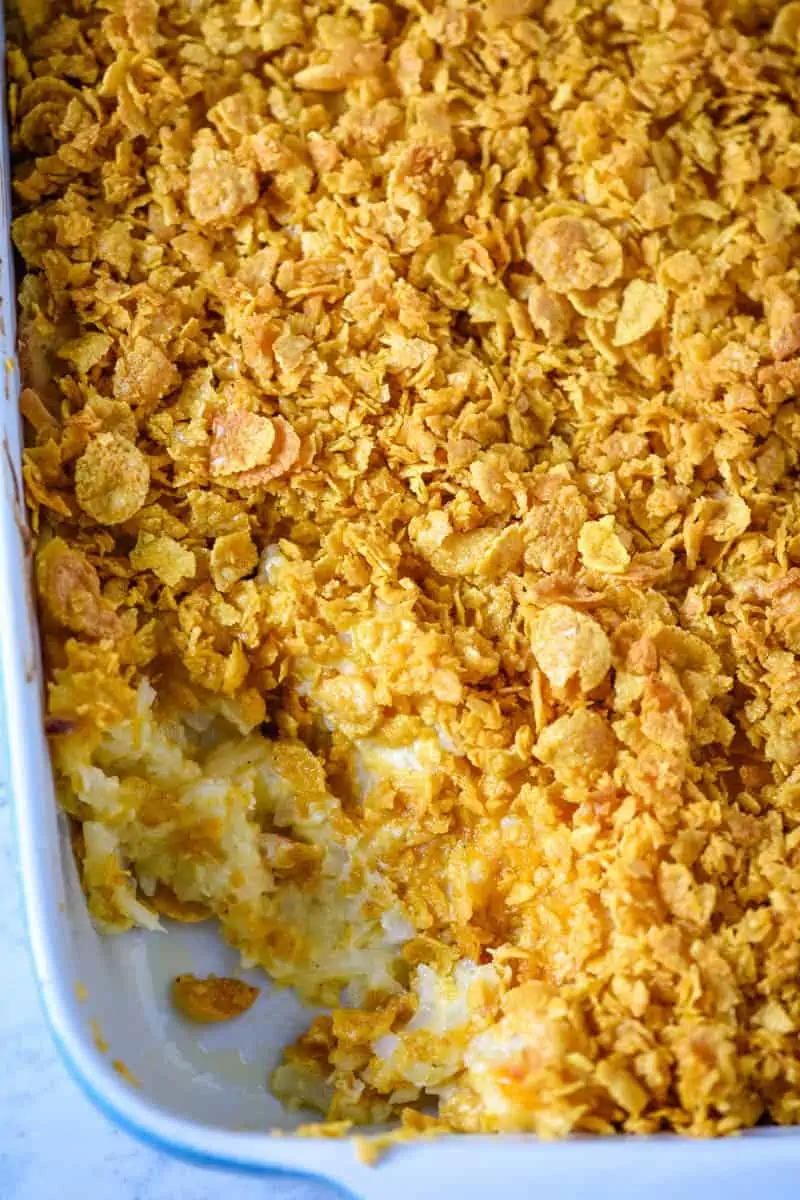 cheesy hash brown potato casserole with Corn Flakes baked in a blue baking dish
