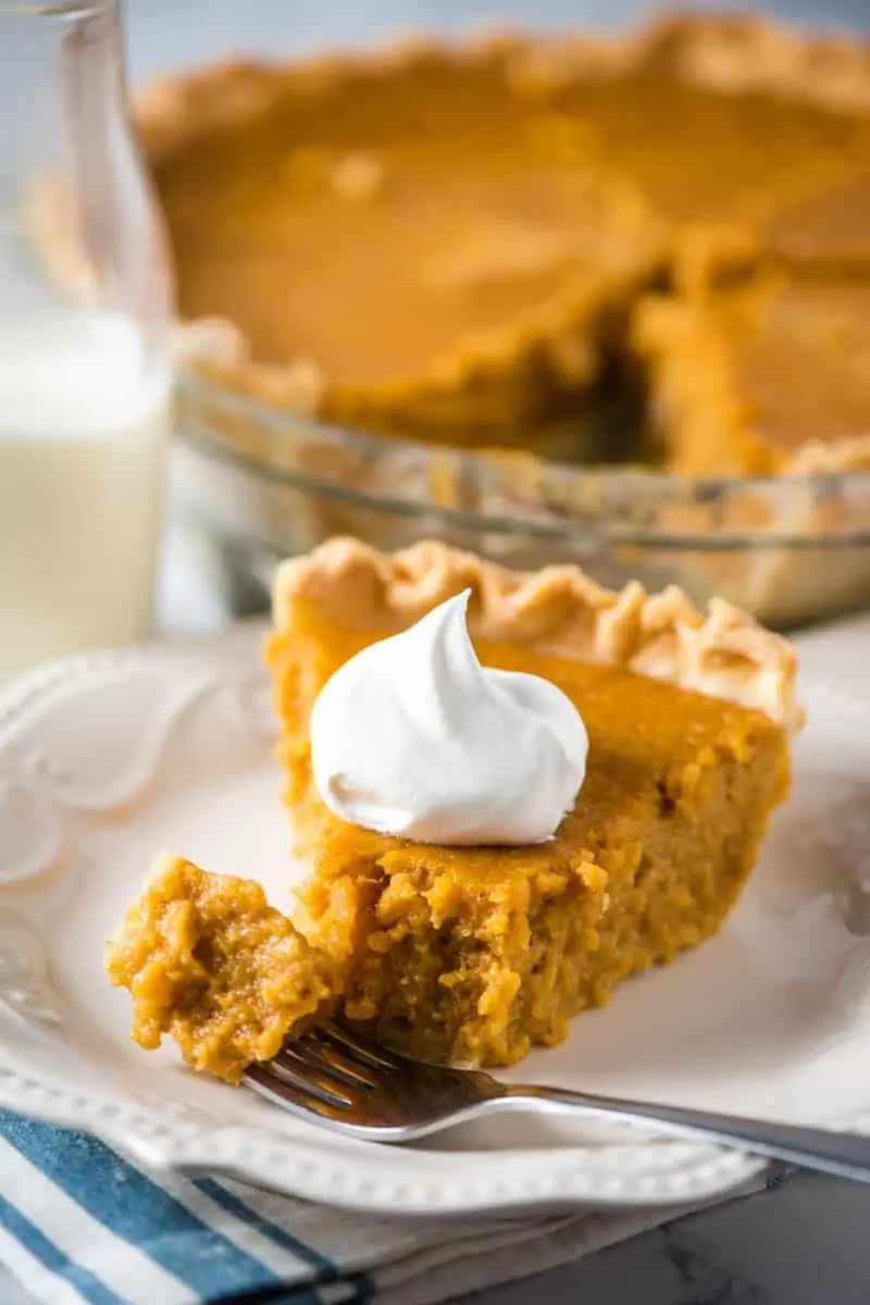 slice of southern style sweet potato pie on white plate with dollop of whipped cream, fork, and bottle of milk