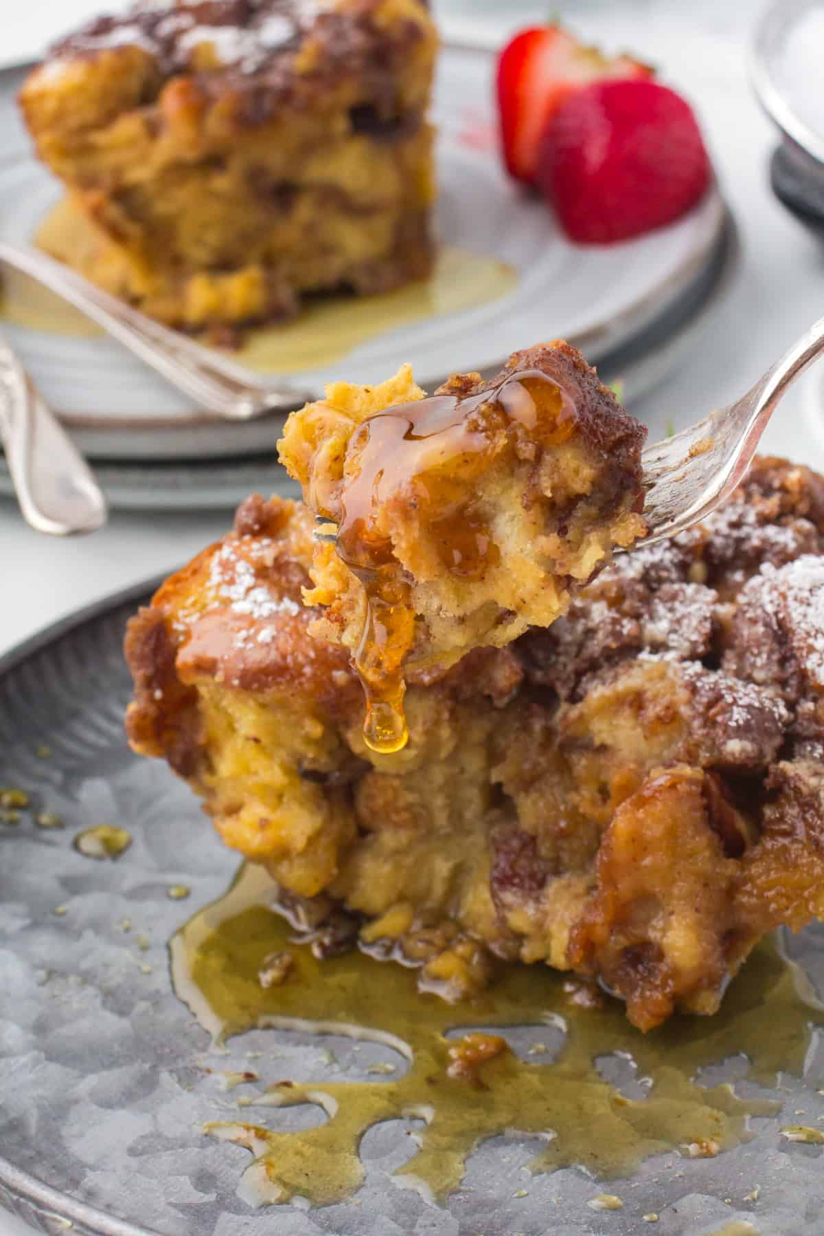 closeup photo showing a forkful of Crock Pot French toast casserole over a gray plate with a slice of French toast casserole