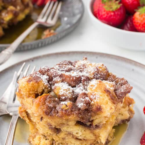 slice of Crockpot French toast casserole served up on a decorative white plate with a pile of fresh strawberries to the side