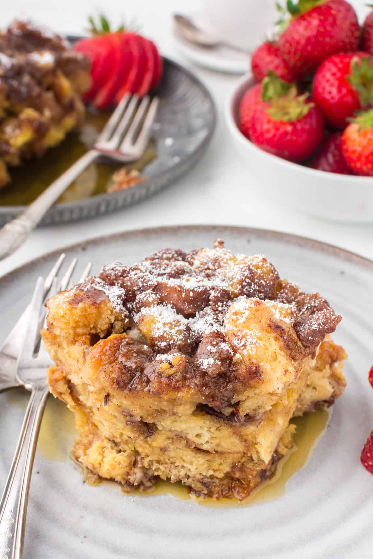slice of Crockpot French toast casserole served up on a decorative white plate with a pile of fresh strawberries to the side