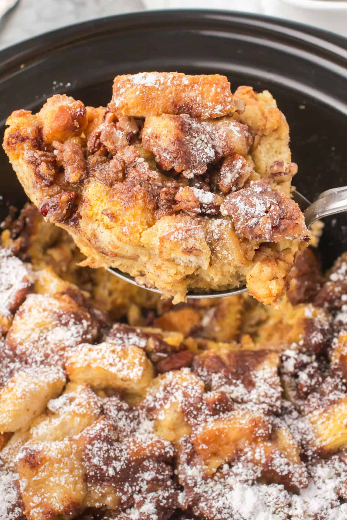 holding up a slice of French toast casserole over a black slow cooker full of French toast casserole