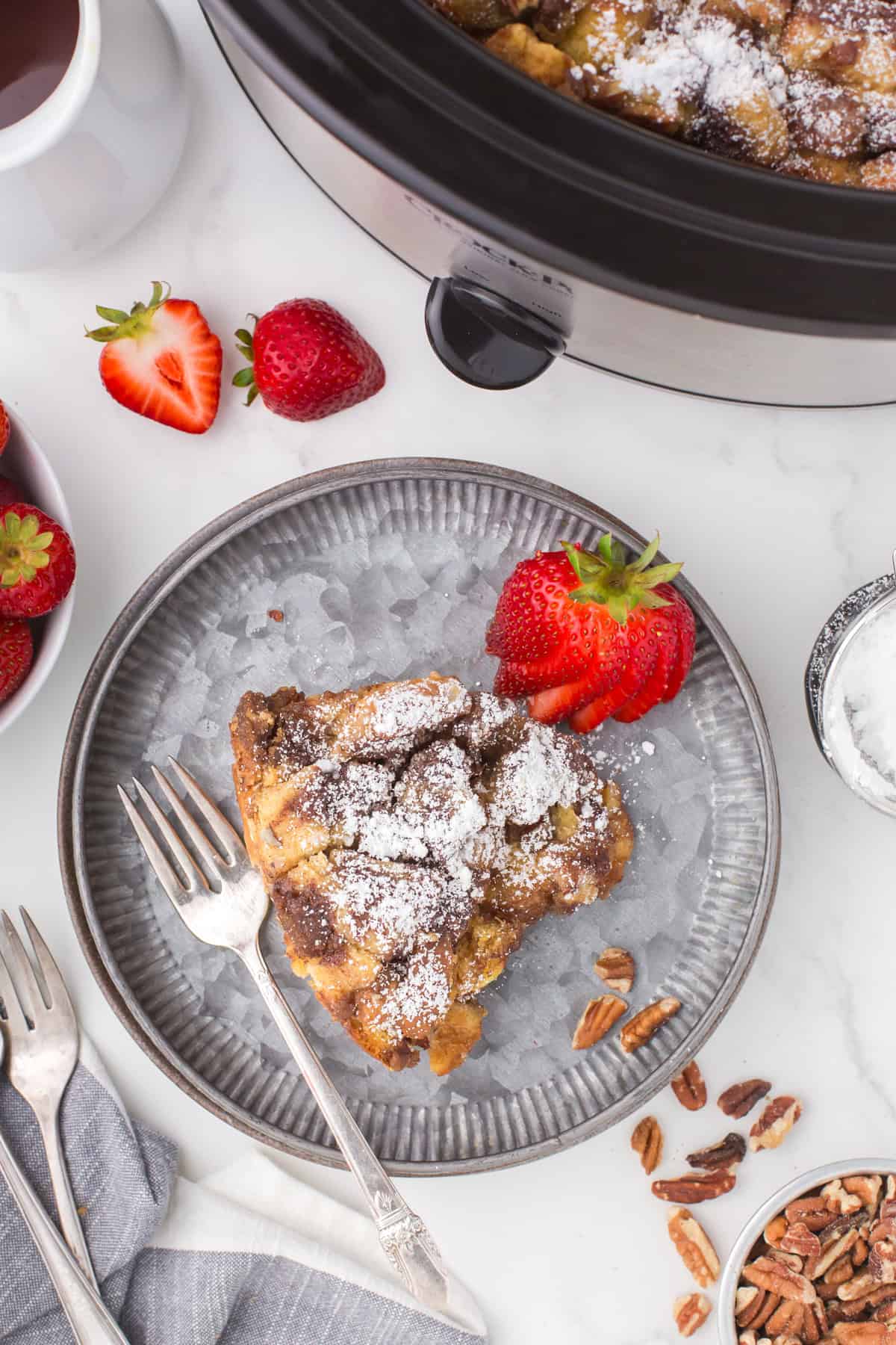 overhead shot showing a slice of slow cooker French toast bake on a small gray plate with a fresh strawberry on the side