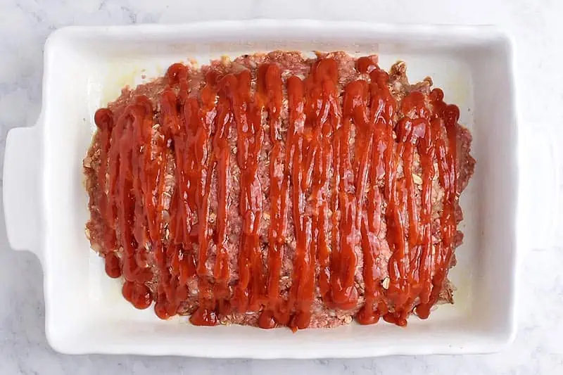 unbaked oatmeal meatloaf covered with ketchup in a white baking dish