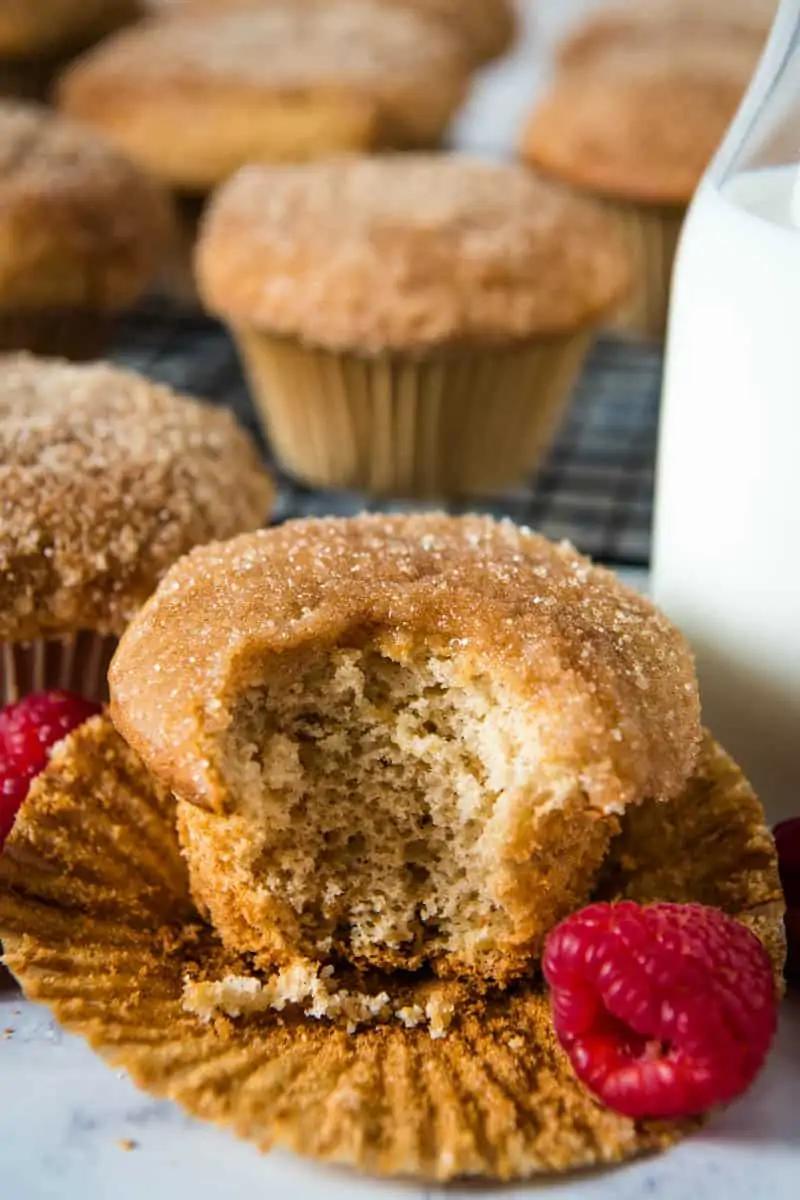 bite out of Bisquick cinnamon muffin sitting on cupcake liner with fresh raspberries and milk in a glass