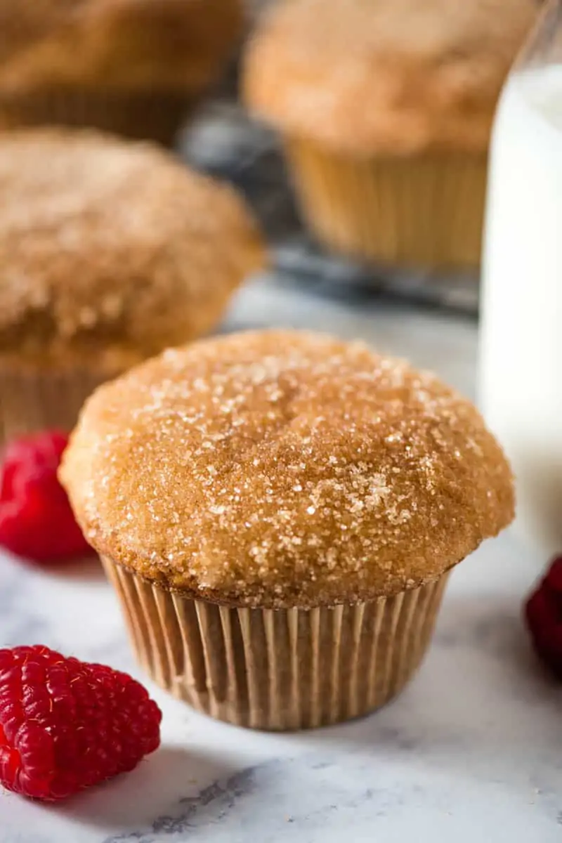 easy cinnamon muffins sitting on white marble countertop with fresh red raspberries and glass of milk