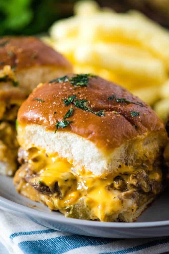 Philly cheesesteak sliders on Hawaiian rolls, sprinkled with Italian parsley, on gray plate with white and blue striped towel