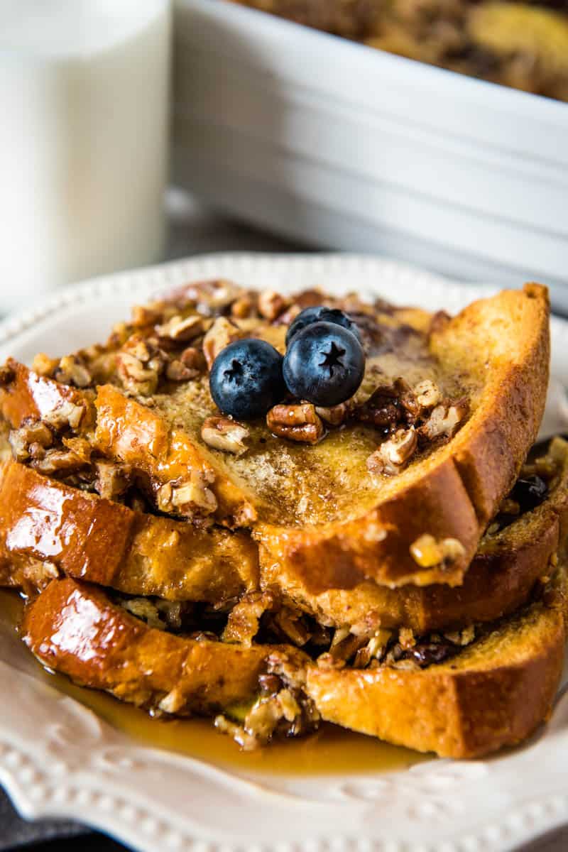 stack of brioche French toast casserole with chopped pecans, fresh blueberries, and maple syrup, on white plate