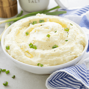 cream cheese mashed potatoes, sprinkled with parsley, in white bowl with blue and white striped towel