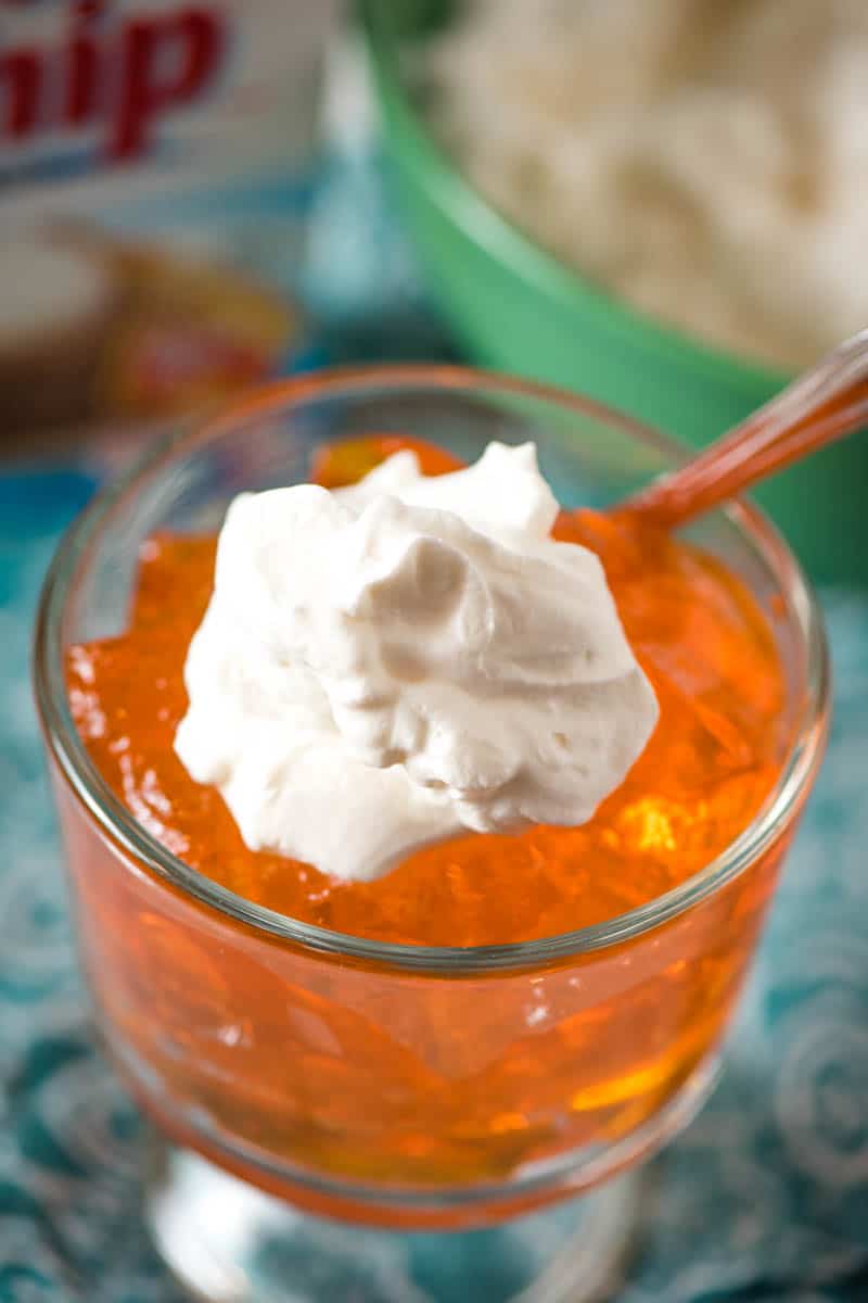 dollop of Dream Whip whipped topping on orange Jello in glass trifle dish with spoon