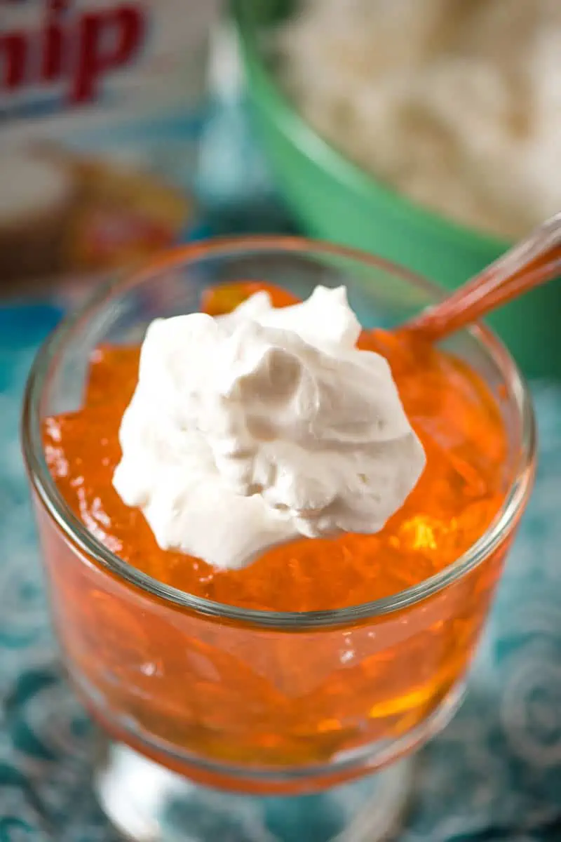 dollop of Dream Whip whipped topping on orange Jello in glass trifle dish with spoon