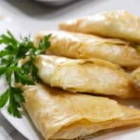 greek cheese triangle pies on white platter with sprig of fresh parsley