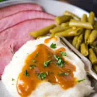 ham gravy with cornstarch on mashed potatoes, served on gray plate with baked ham, green beans, and a fork
