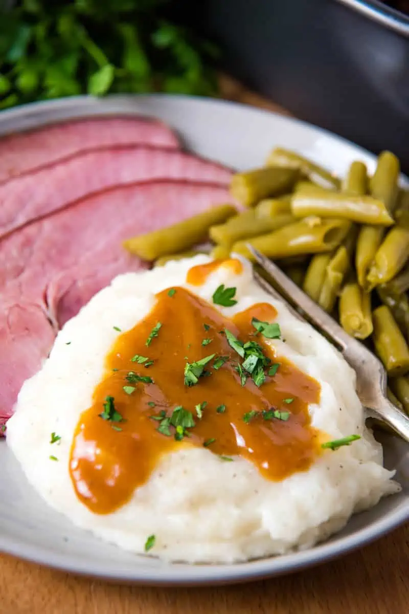 ham gravy with cornstarch on mashed potatoes, served on grate plate with baked ham, green beans, and a fork