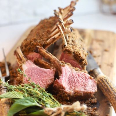 roasted rack of lamb with garlic and herbs on wooden cutting board with knife
