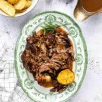 slow cooker leg of lamb on green and white plate on white marble countertop