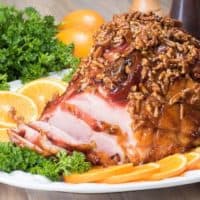 southern pecan glazed ham on white platter with orange slices and fresh parsley