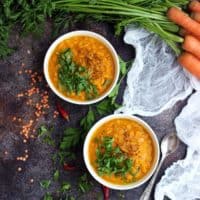vegan roasted carrot soup with lentils in white bowls on dark gray countertop with white kitchen towel and fresh parsley