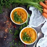 vegan roasted carrot soup with lentils in white bowls on dark gray countertop with white kitchen towel and fresh parsley