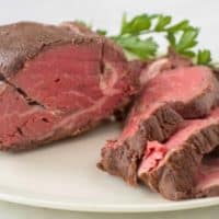 sous vide beef tenderloin sliced on white platter with fresh herbs