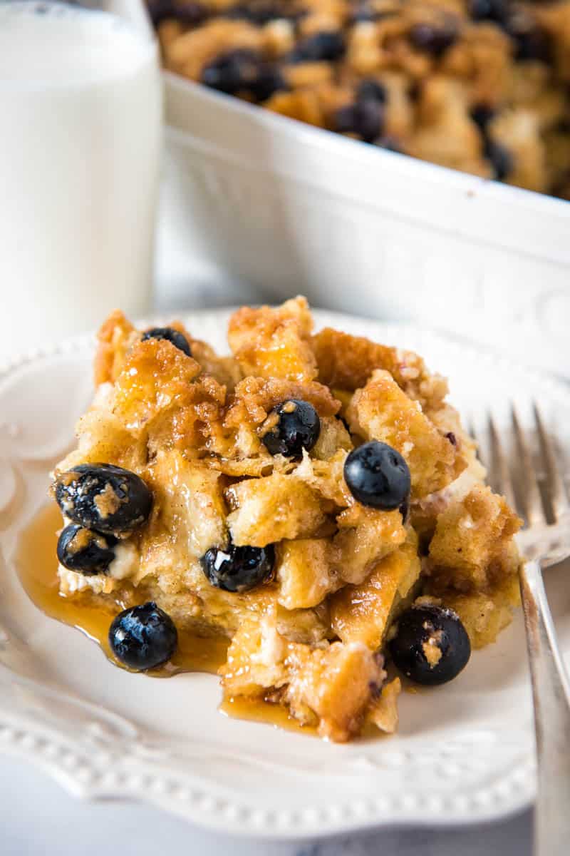 slice of blueberry French toast bake on white plate with fork and topped with maple syrup