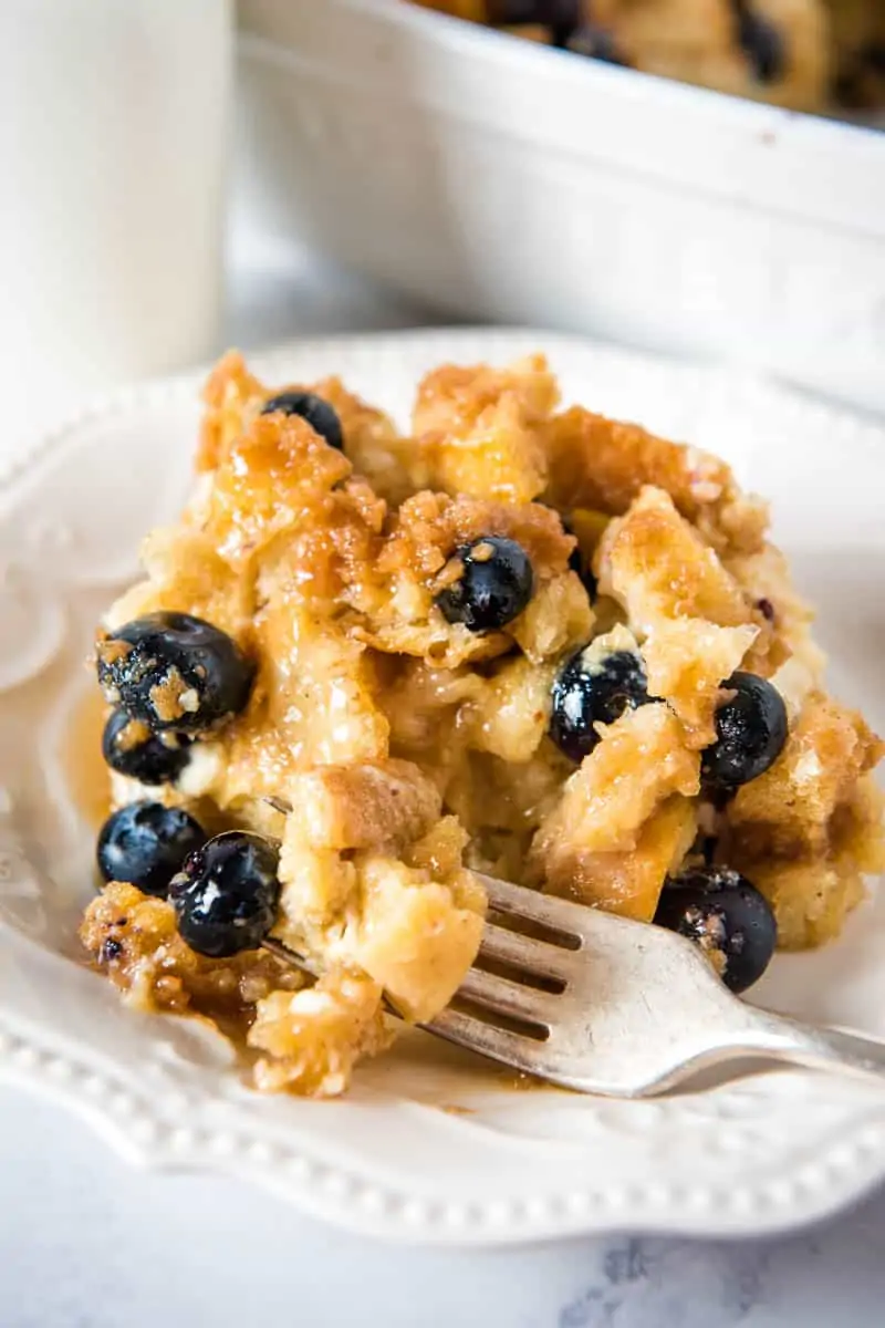 serving of blueberry French toast casserole with bite on fork, on white plate